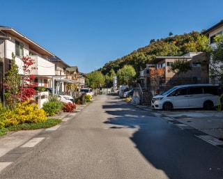 両側に戸建て住宅が並び、奥には緑豊かな山並みが見える整った街並み
